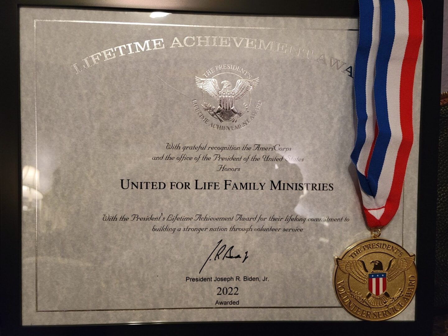 A medal and certificate are displayed in front of the united for life family ministries sign.