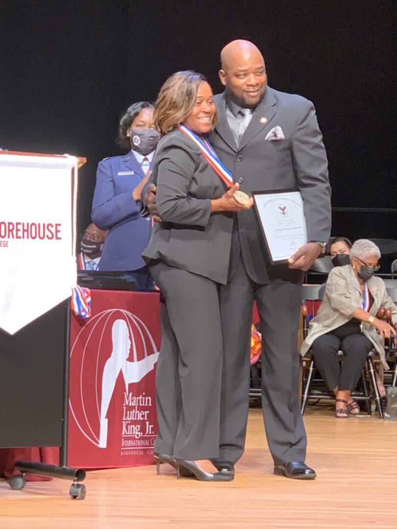 A man and woman are standing on stage holding papers.