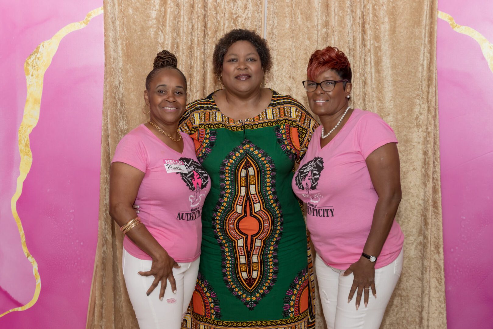 Three women posing for a picture in front of a curtain.